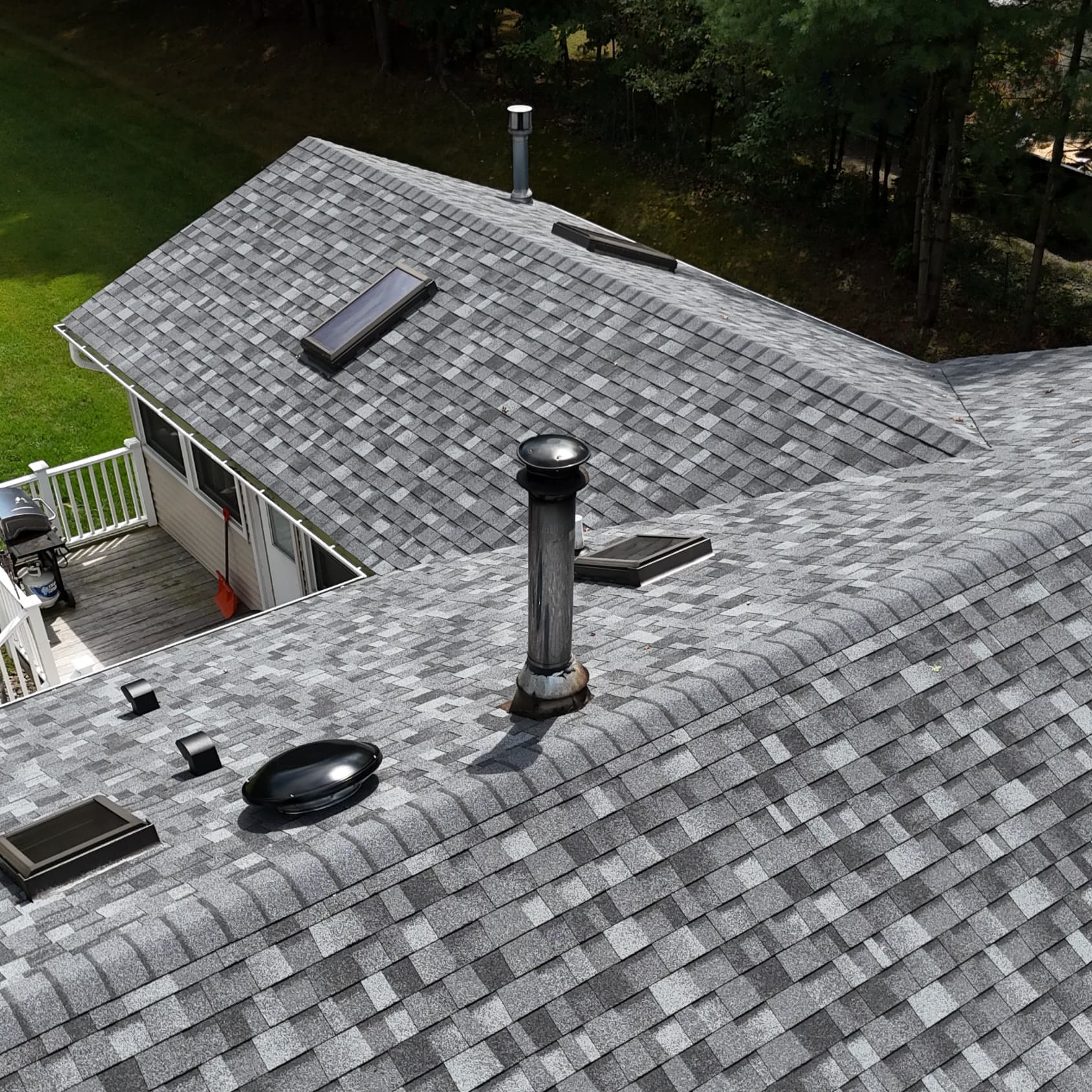 Close up of a new gray shingle roof with vents and a skylight